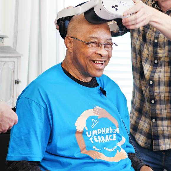 Elderly man smiles as a white VR headset is removed from his head.