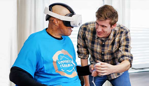 Elderly man uses a VR headset and controller with male healthcare workers.